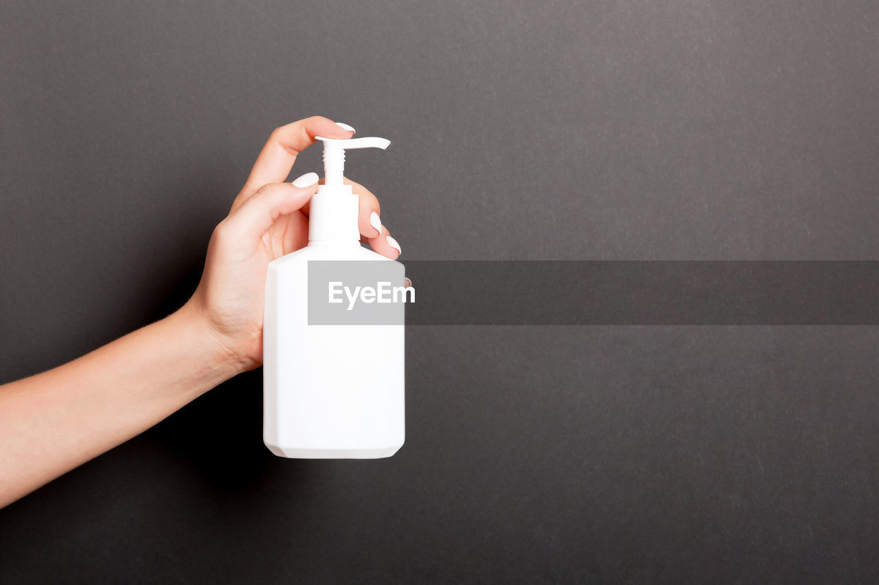 Close-up of human hand holding soap dispenser bottle against black background