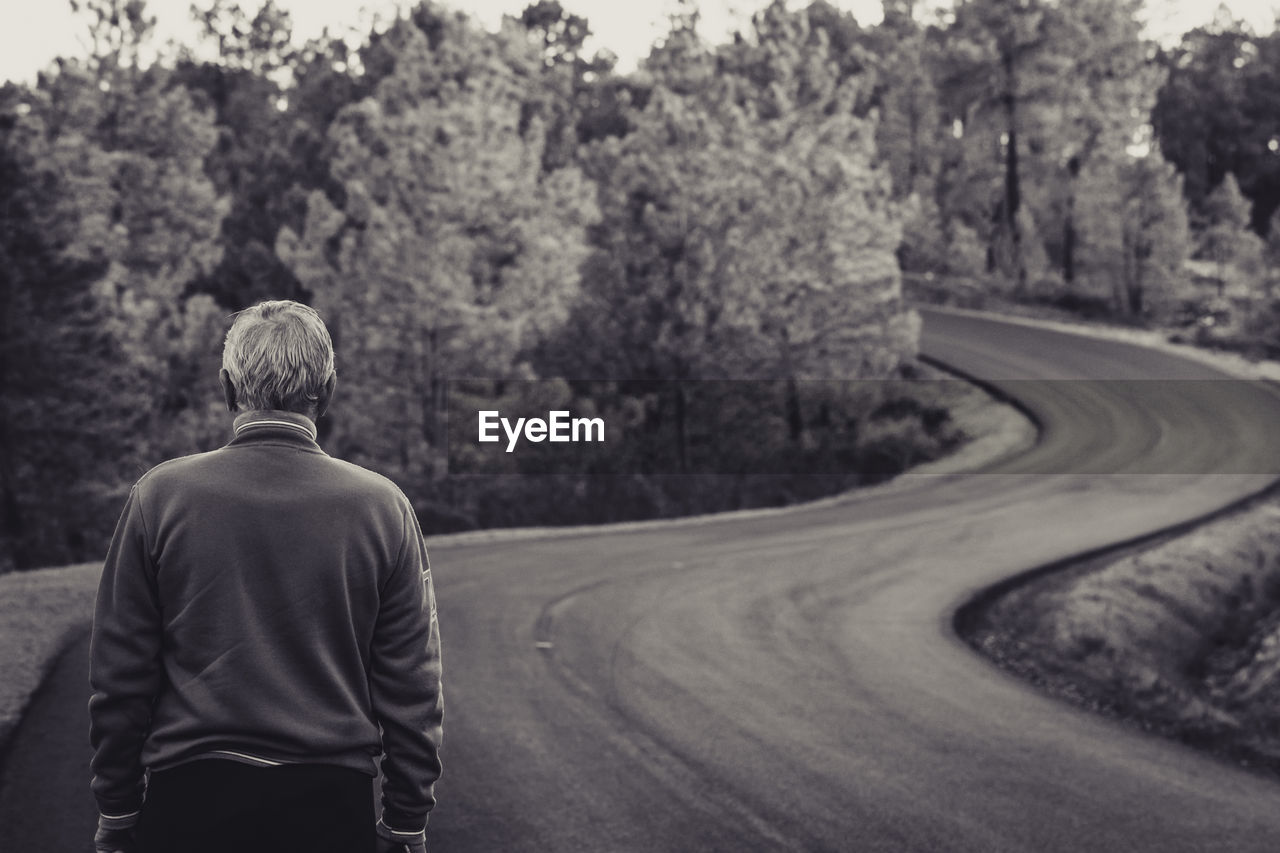 Rear view of senior man standing on road against trees in forest