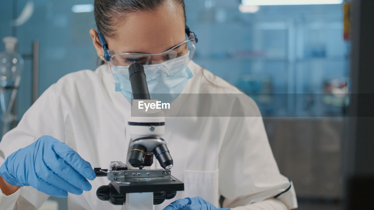 Scientist wearing mask looking through microscope