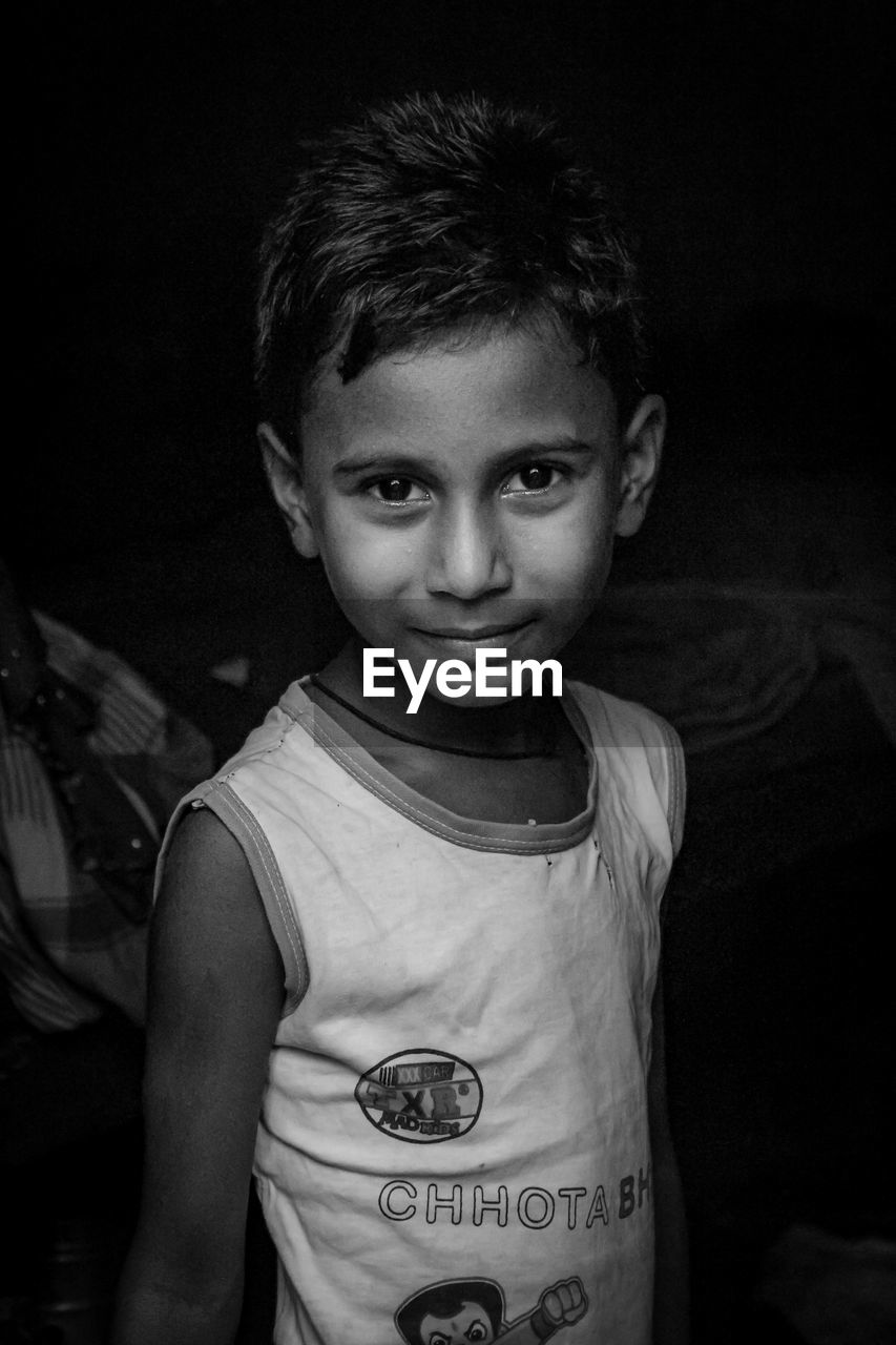 PORTRAIT OF BOY STANDING BY BLACK BACKGROUND