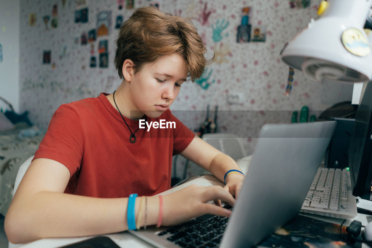 A teenage girl is studying online using a laptop while sitting at a table in the room.