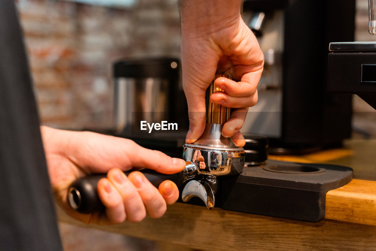 Crop unrecognizable barista pressing coffee in portafilter with tamper while preparing beverage in cafe