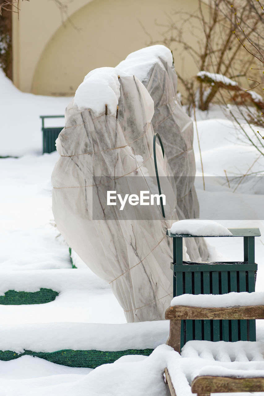 Plants and trees in a park or garden covered by the snow and blanket, swath of burlap