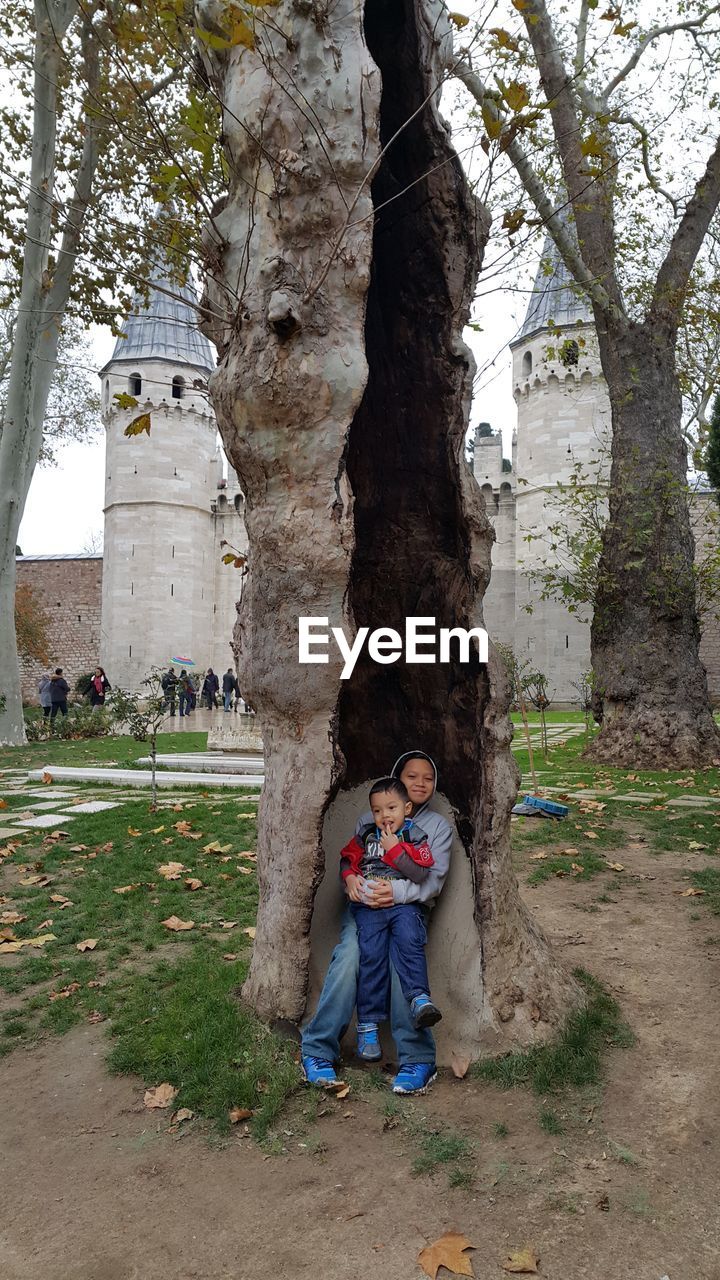 Portrait of siblings embracing while standing against tree trunk 