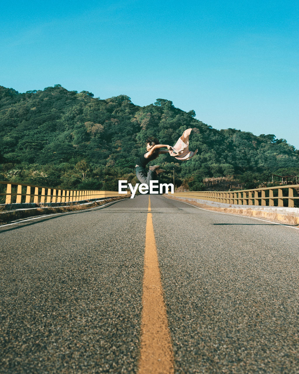 Woman jumping on road against clear sky