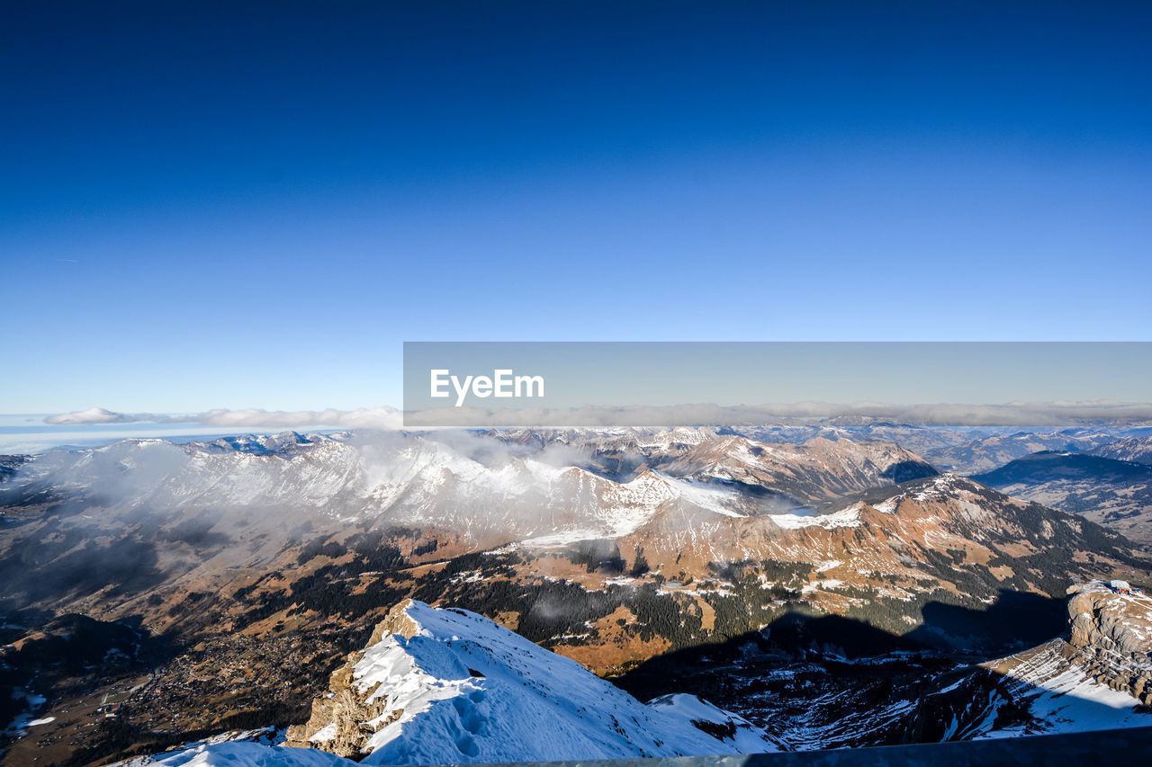 Aerial view of snowcapped mountain against blue sky
