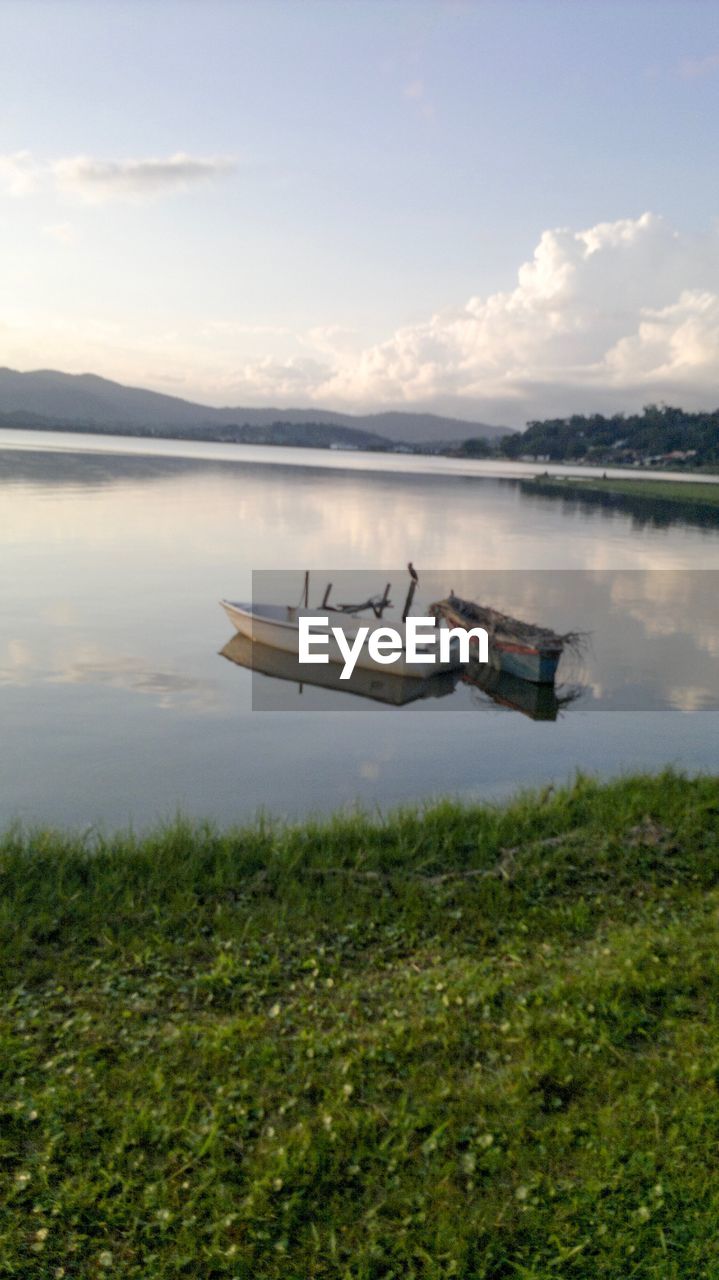 BOATS MOORED ON LAKE AGAINST SKY