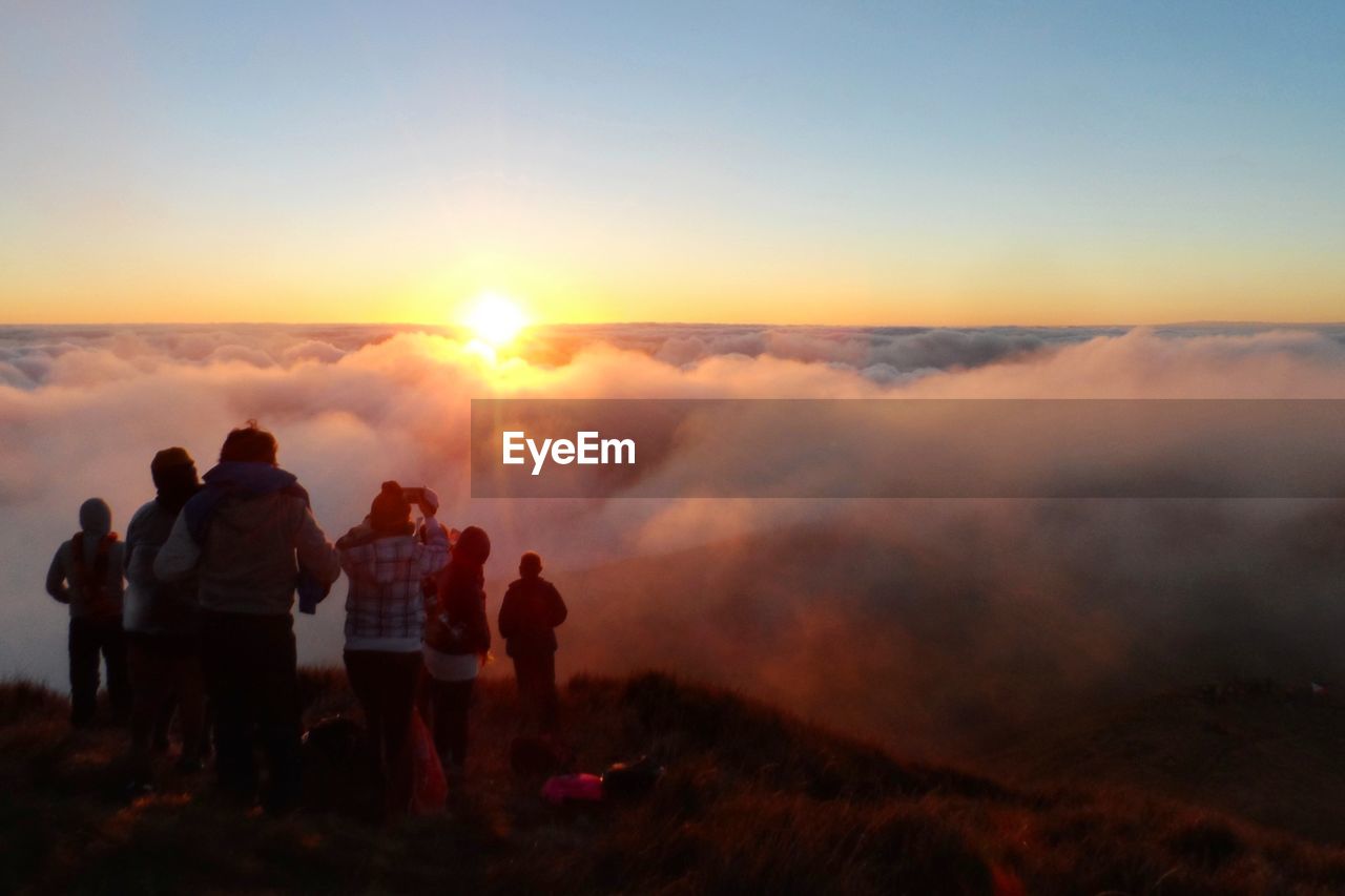 People standing on mountain against cloudscape during sunset