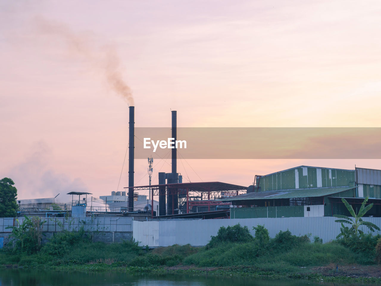 Industry factory building with smoke and steam from smokestack near river against twilight sky