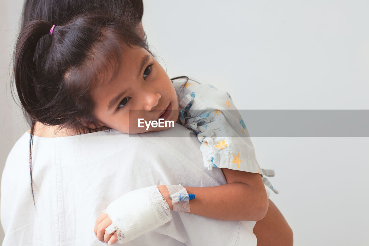 Mother carrying sick daughter against wall in hospital