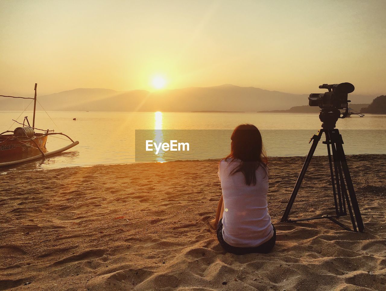 Woman sitting on beach at sunset