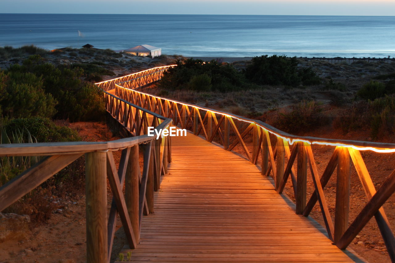 Empty illuminated boardwalk leading towards beach at dusk