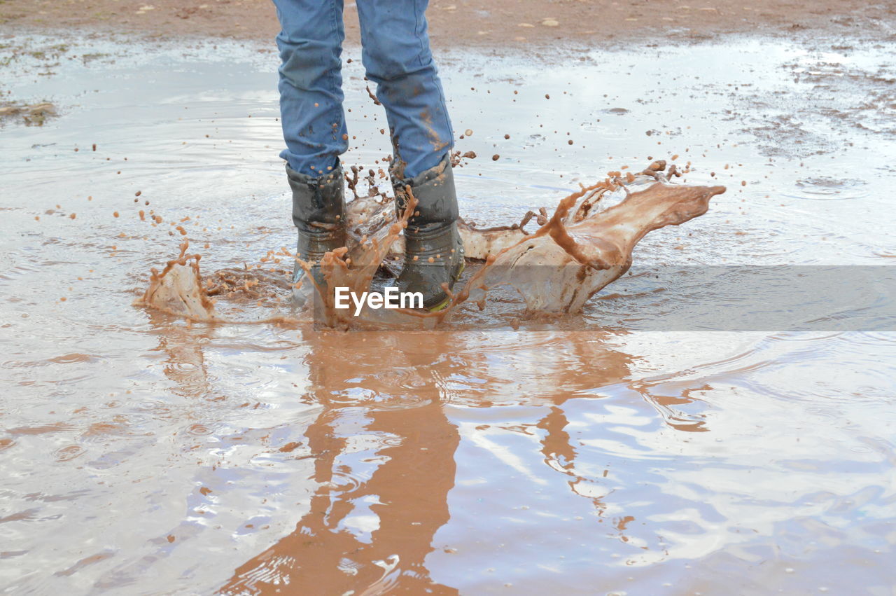 Low section of person splashing muddy puddle