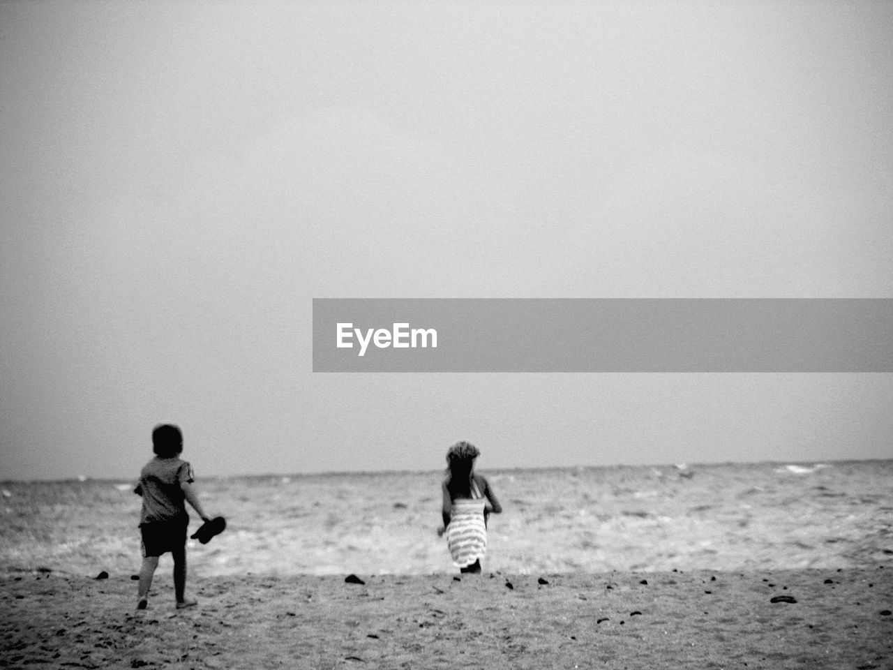 Rear view of children running at beach against clear sky