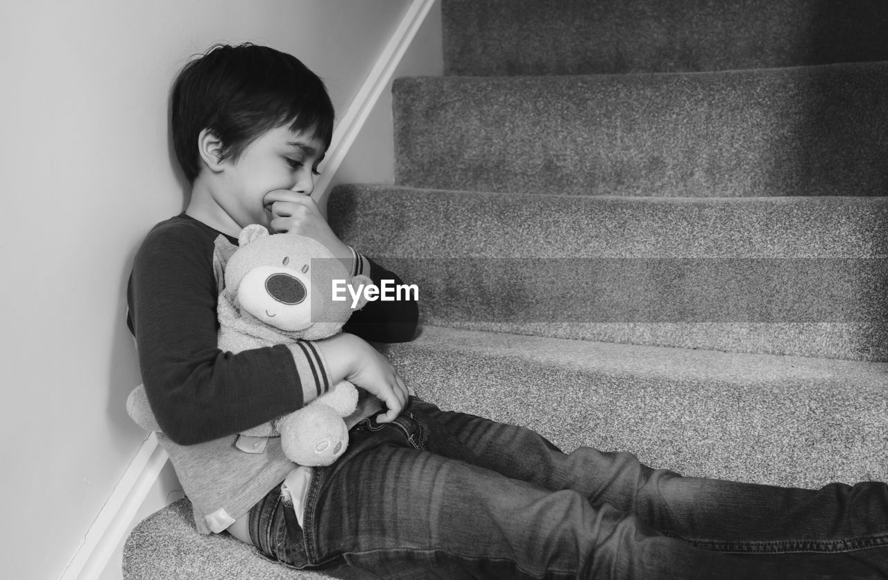 Boy holding teddy bear while sitting on steps