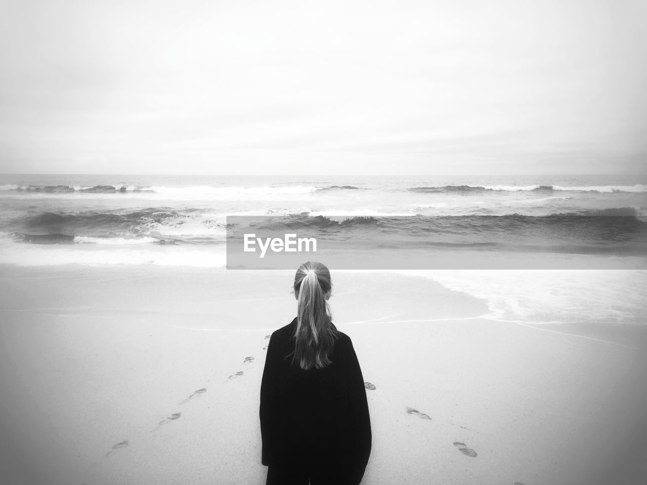 Rear view of woman standing at beach against clear sky