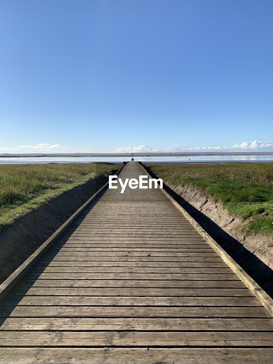 Wooden walkway leading out to the sea with a blue sky background 