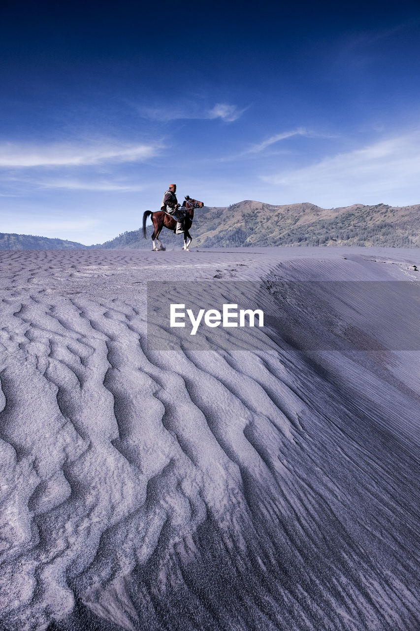 Mid adult man riding horse at desert against sky