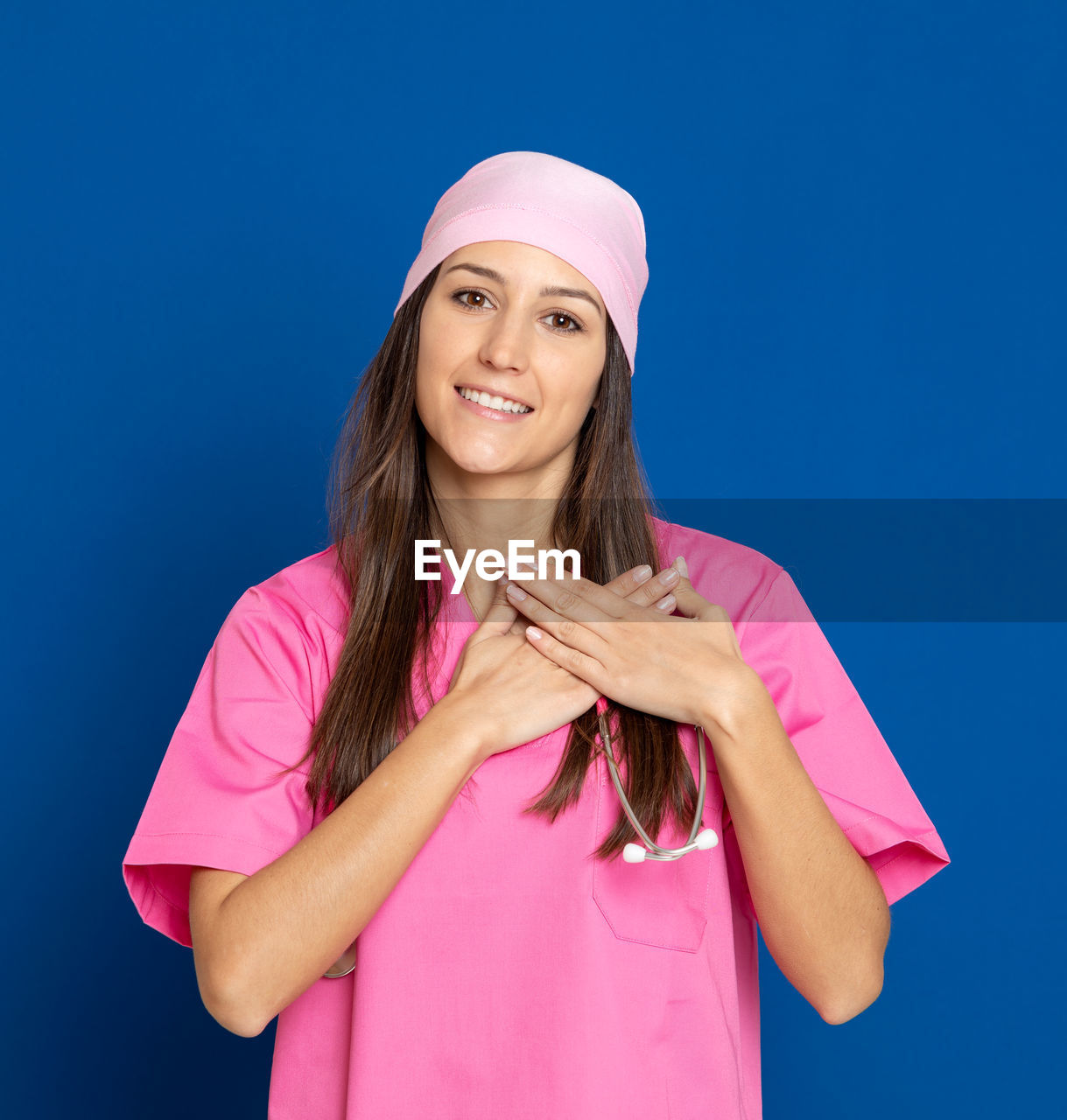 PORTRAIT OF SMILING YOUNG WOMAN STANDING AGAINST BLUE BACKGROUND