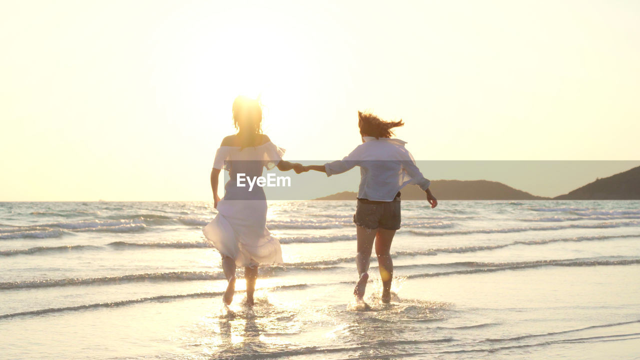 Rear view of two women walking on beach against sky