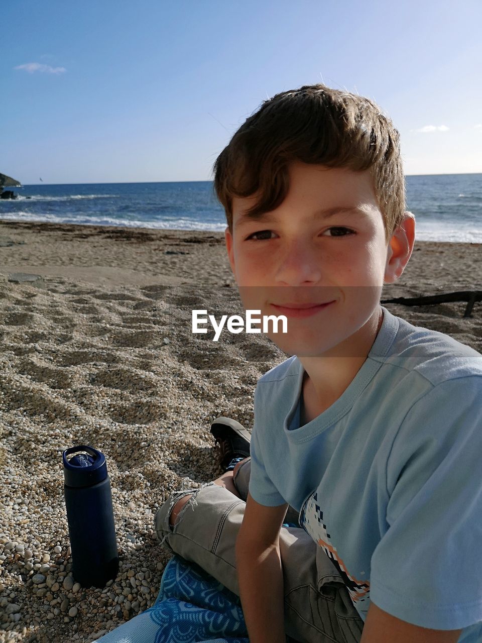 Portrait of boy sitting on shore at beach against sky