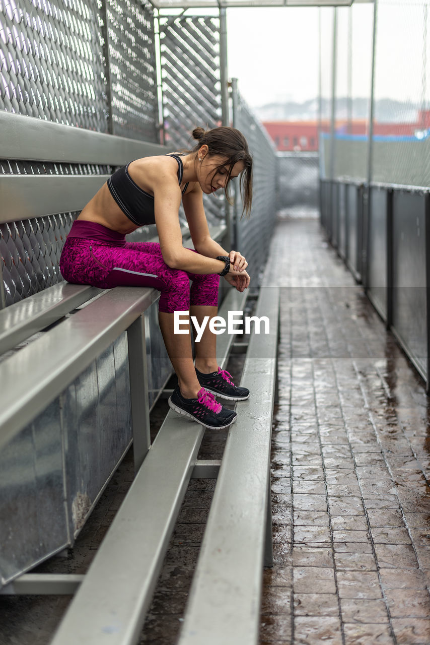 Side view full body of toned female athlete in activewear sitting on bench after outdoor workout