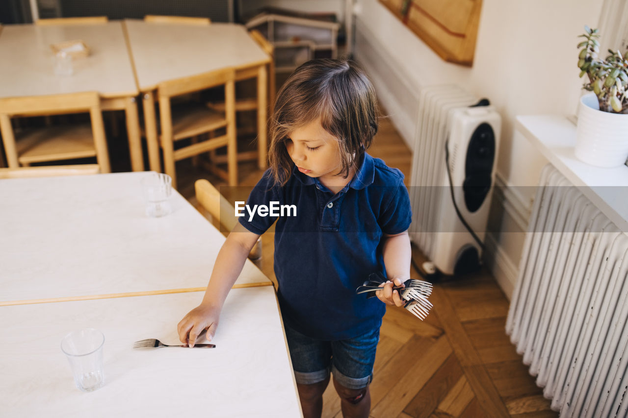 High angle view of boy arranging fork on table in child care classroom