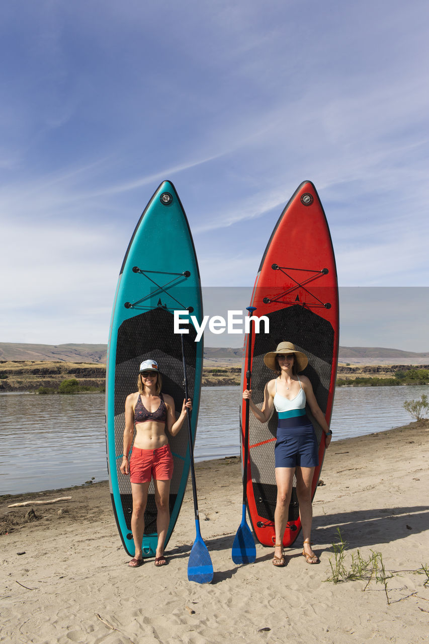 Two women stand in front of their sups near the columbia river in or.