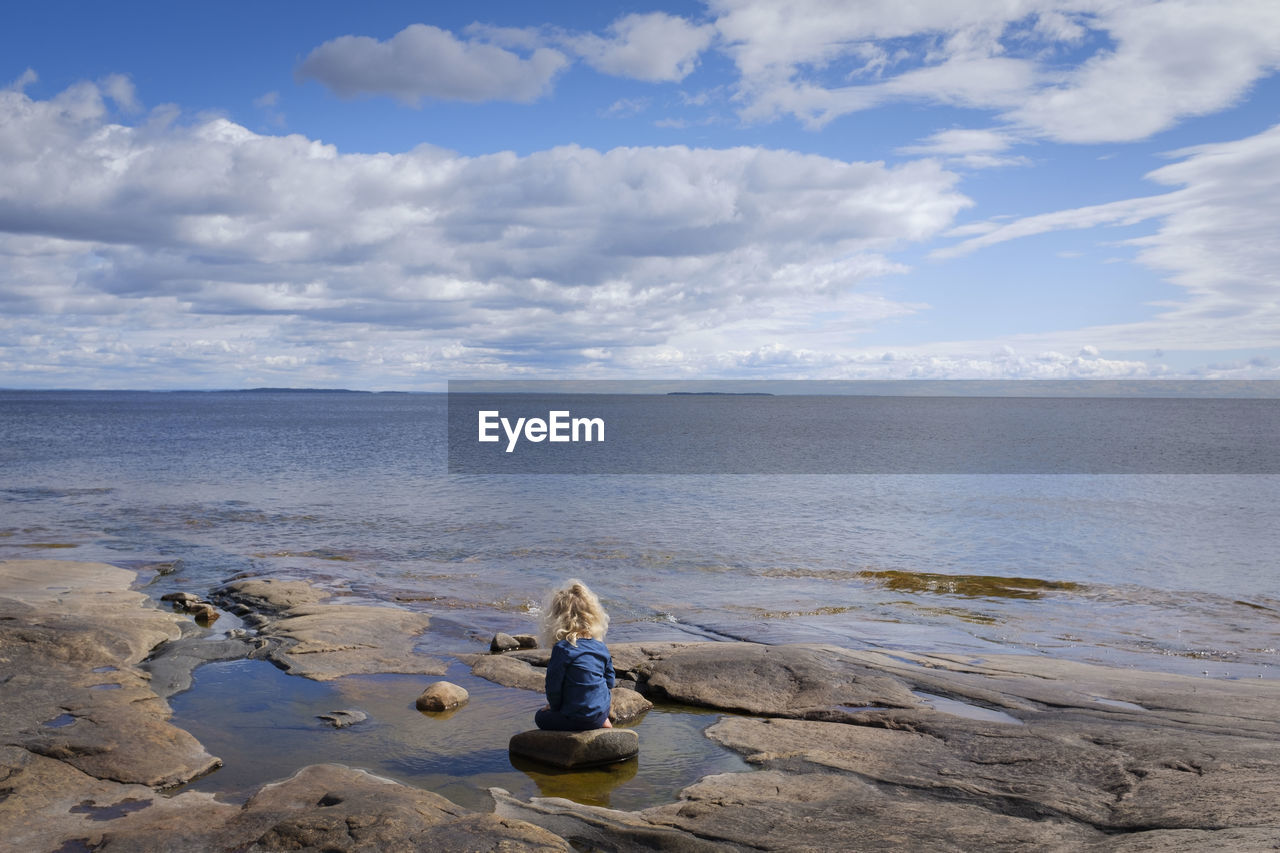 Toddler sitting on rocks looking out at water 
