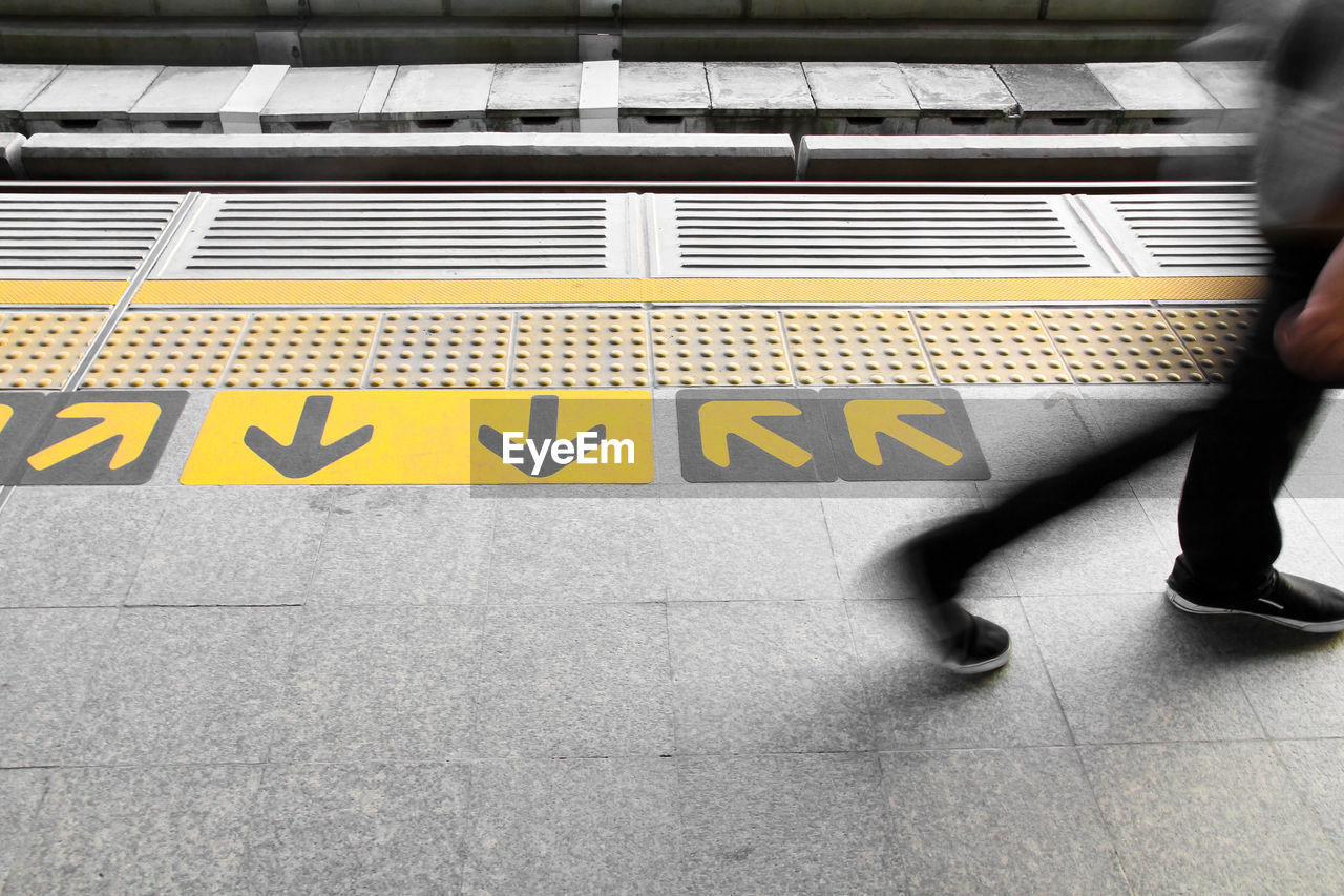 LOW SECTION OF MAN WALKING ON YELLOW TEXT ON STREET