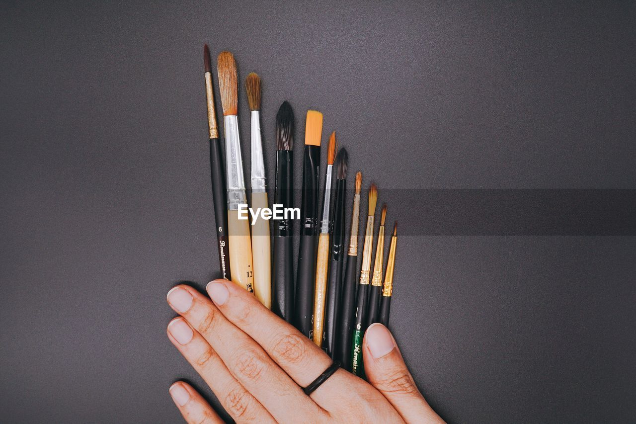 Cropped hand of person holding paintbrushes on black table