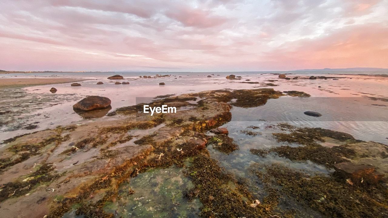 Rocks on beach against sky during sunset