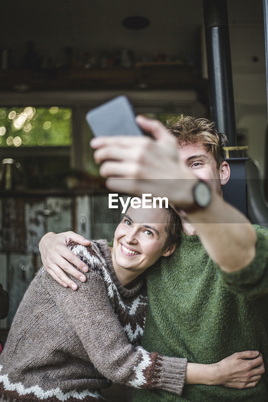 Smiling man taking selfie with woman from mobile phone during camping