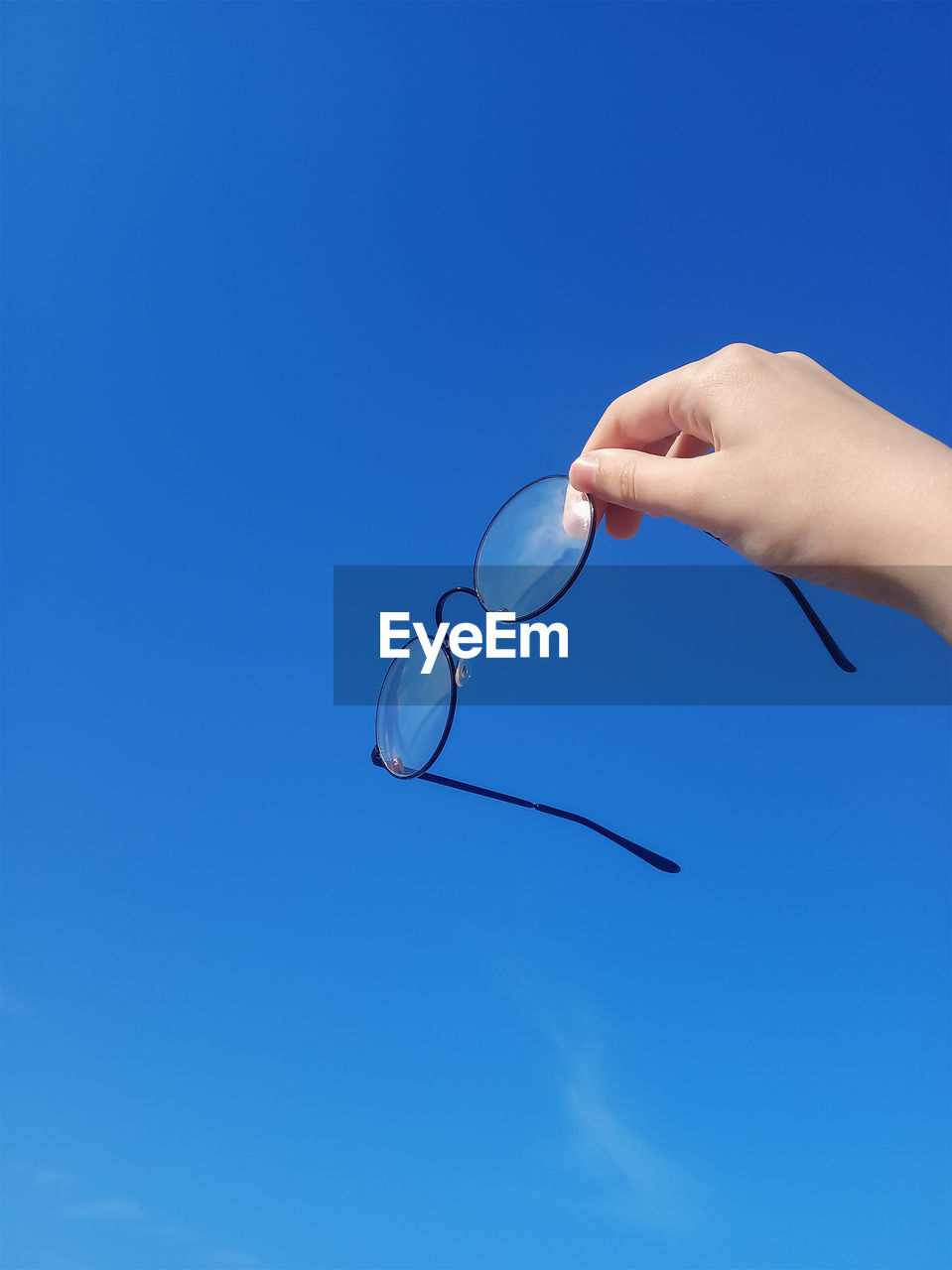 Transparent glasses in a black frame, in his hand, raised up against the blue sky