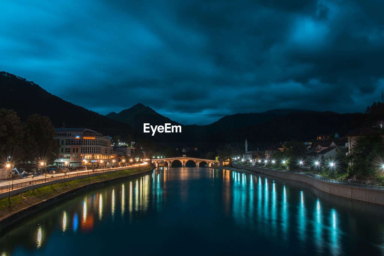Illuminated bridge over river against sky at night