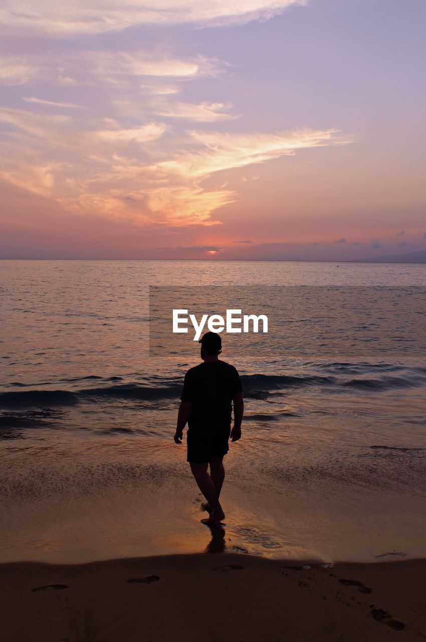 Man wading in sea against sky during sunset