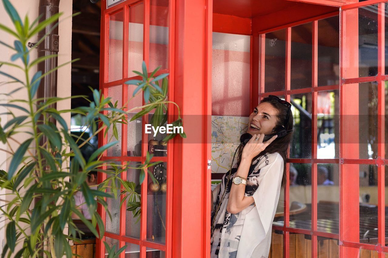 Woman talking on telephone while standing in booth