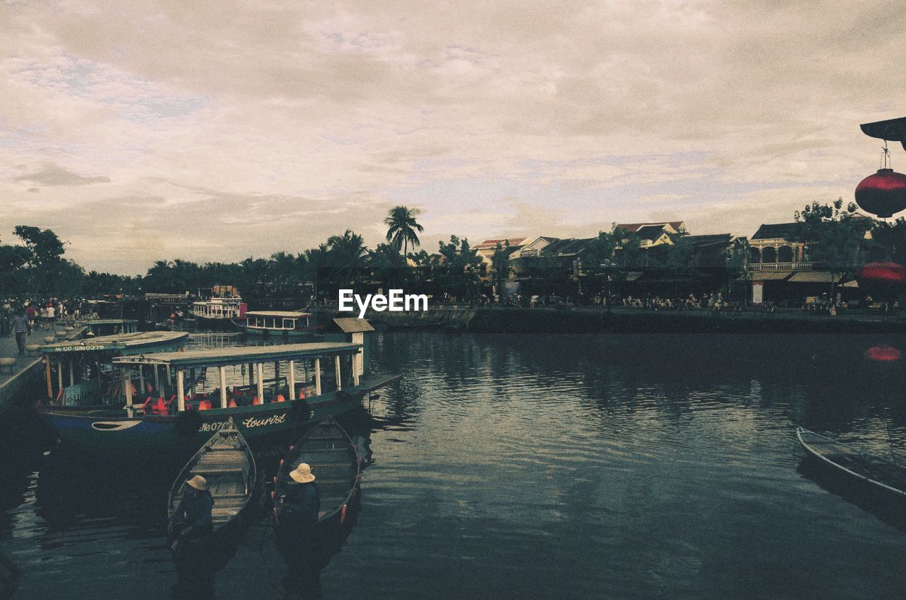 BOATS IN CALM RIVER ALONG BUILDINGS