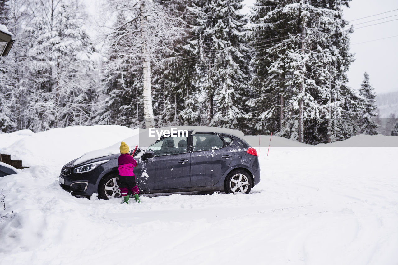 Girl brushing snow from car