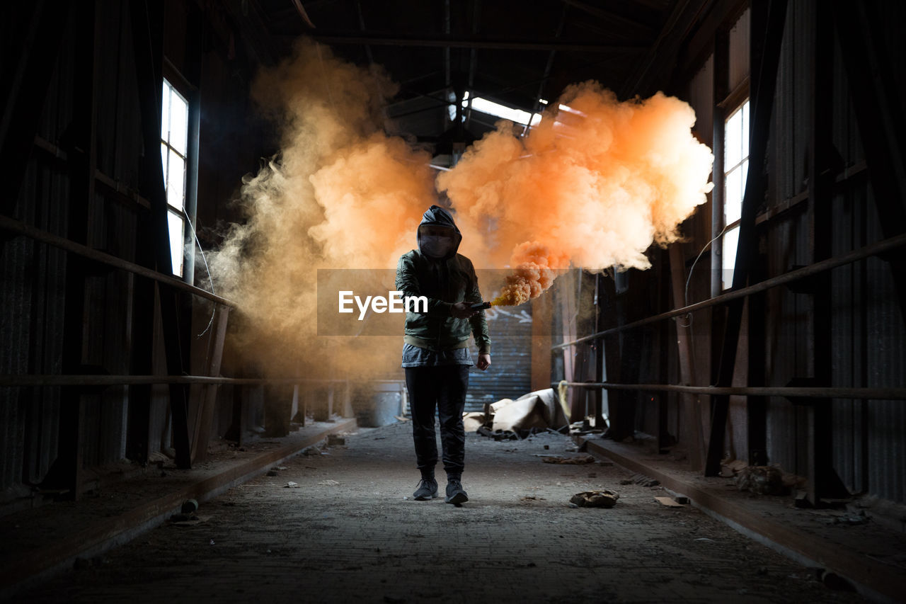 Full length of man holding distress flare while walking in abandoned workshop