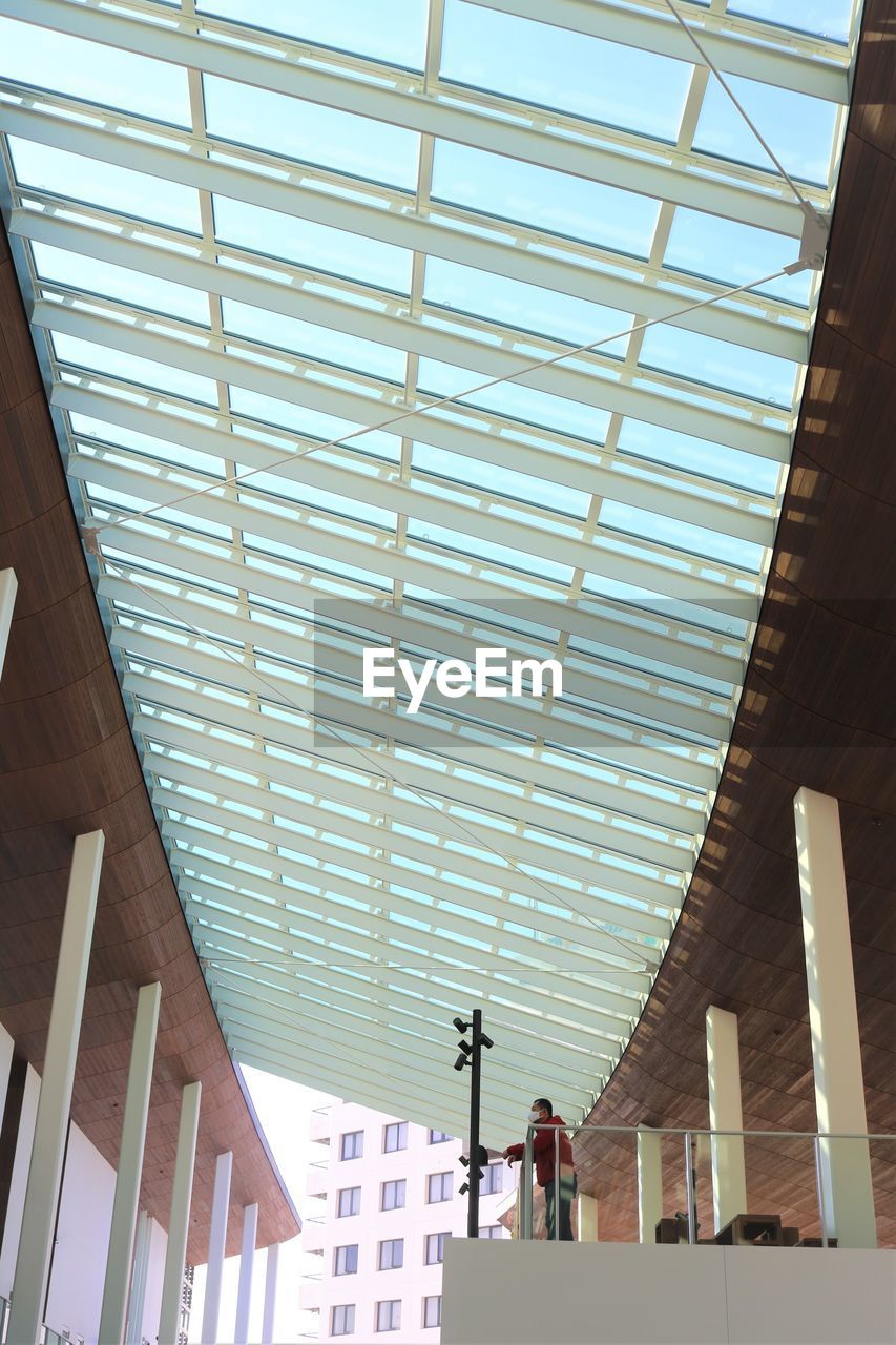 Low angle view ofperson standing below skylight in building against sky