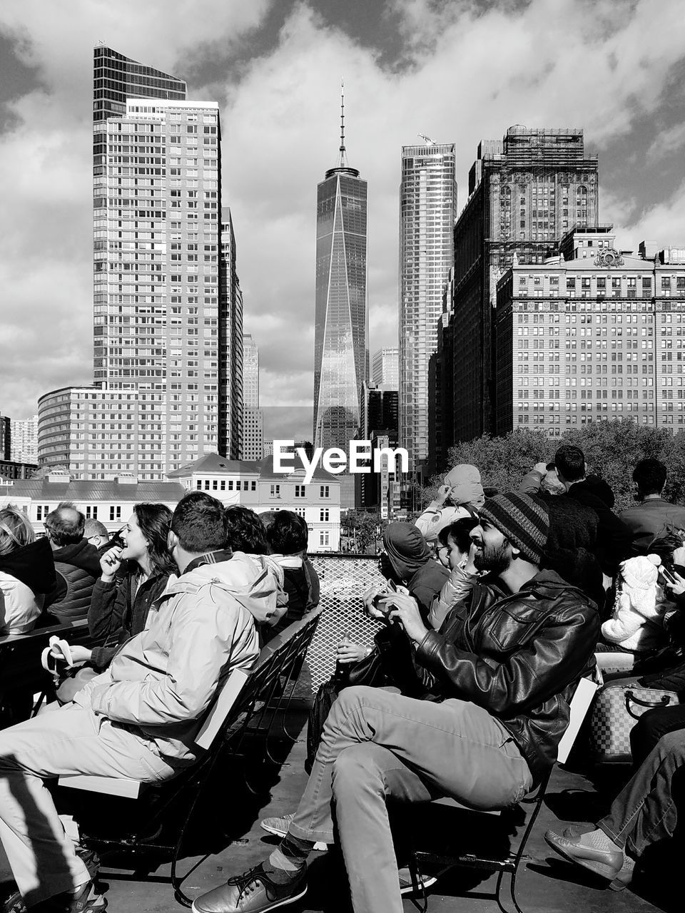 Tourists sitting on chairs at promenade against one world trade center
