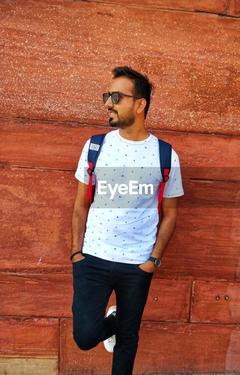 Young man looking away while standing against wall