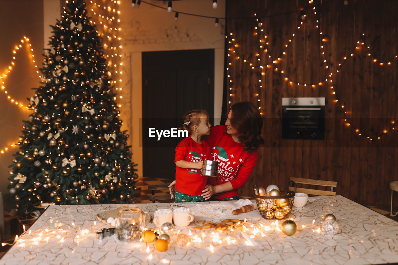 Cheerful parents and a child in red pajamas prepare christmas cookies in the decorated kitchen