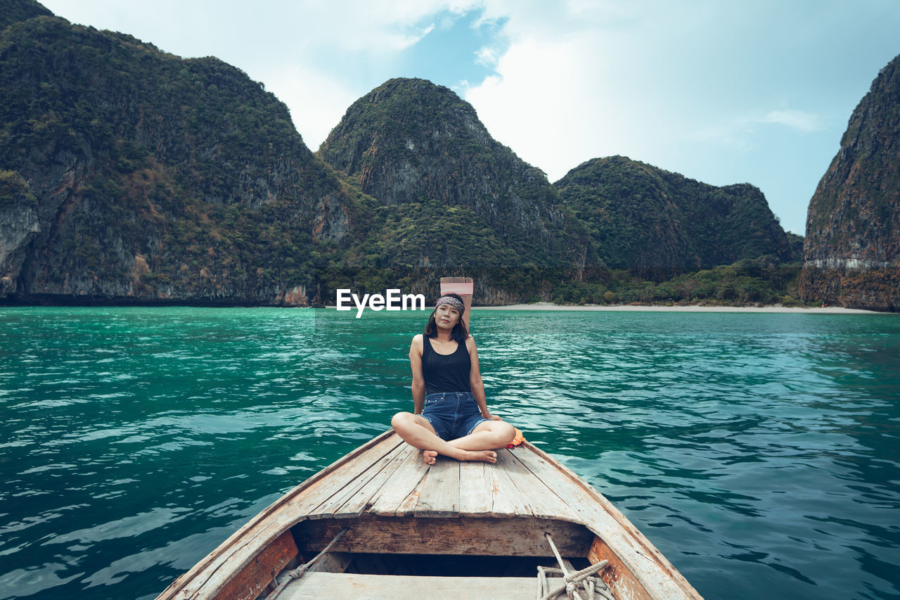 Full length of woman sitting on boat in sea against mountains