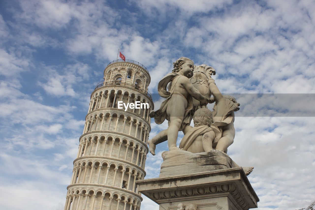 Statues and leaning tower of pisa against cloudy sky