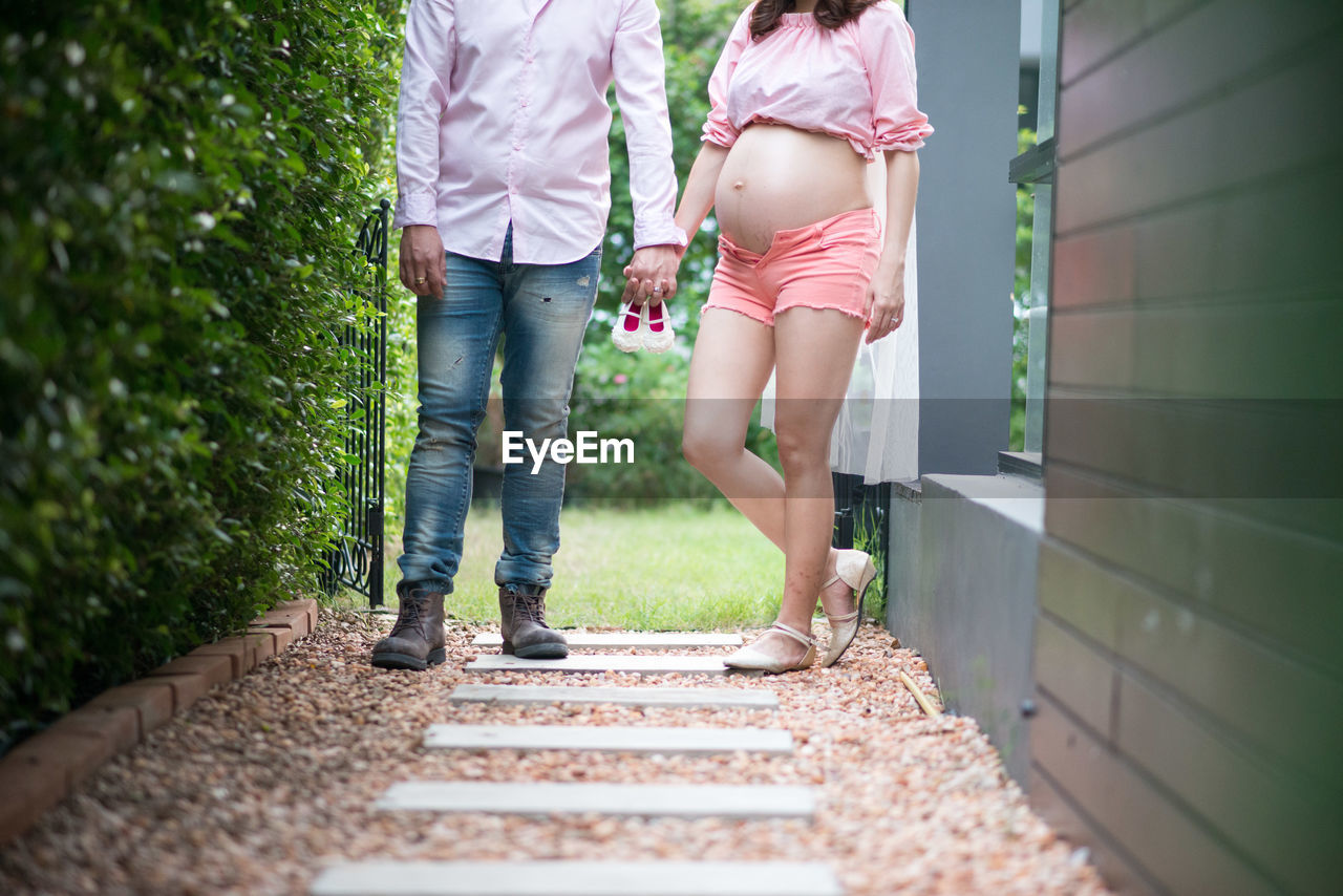 Low section of couple standing on footpath while holding hands