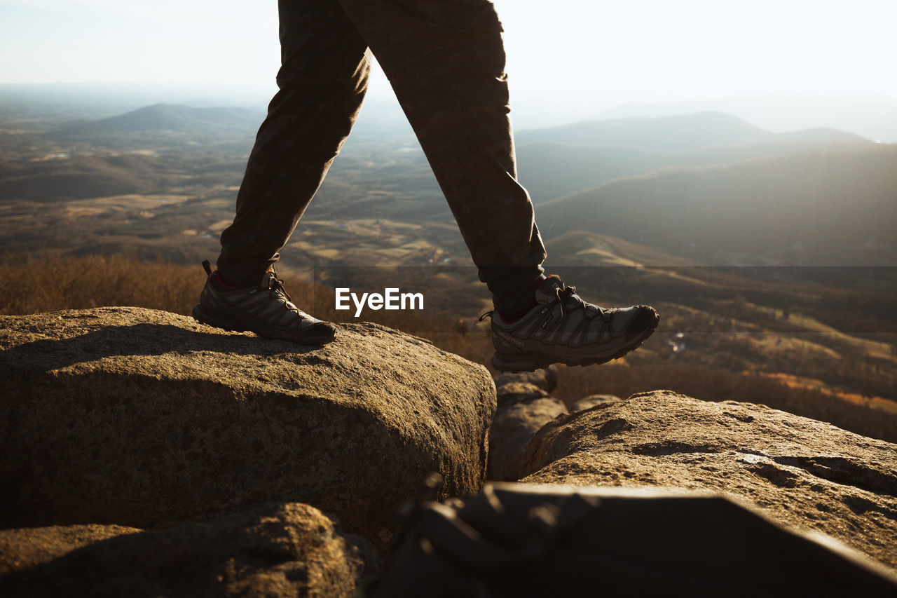 Low section of man walking on rocks against mountains