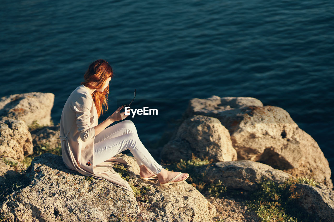 Woman sitting on rock by sea