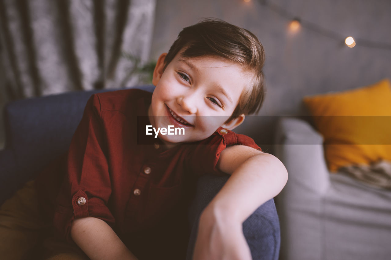 Portrait of smiling cute boy sitting on chair at home